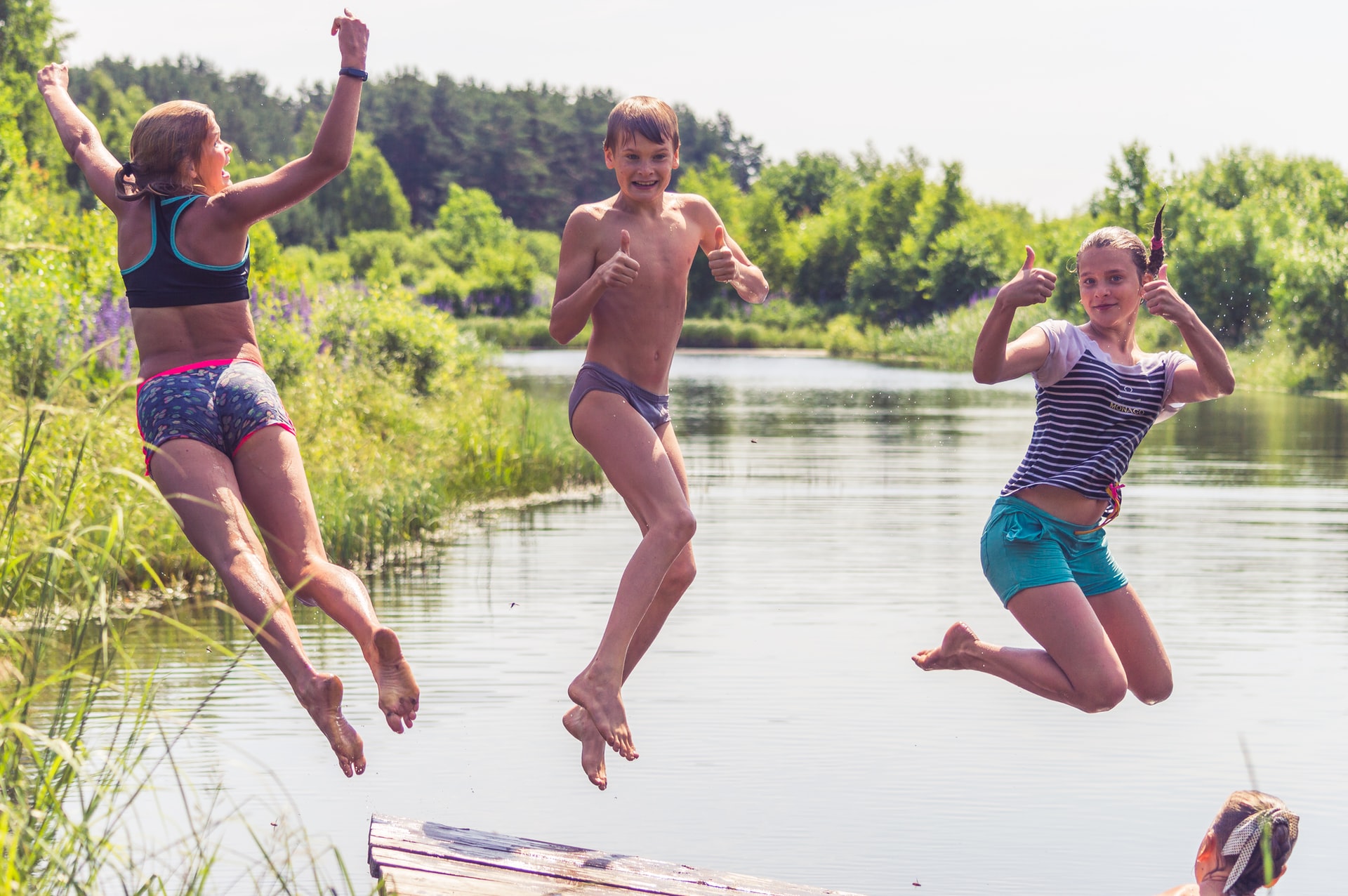 Three children in swimming costumes jumping into a lake, in the summer